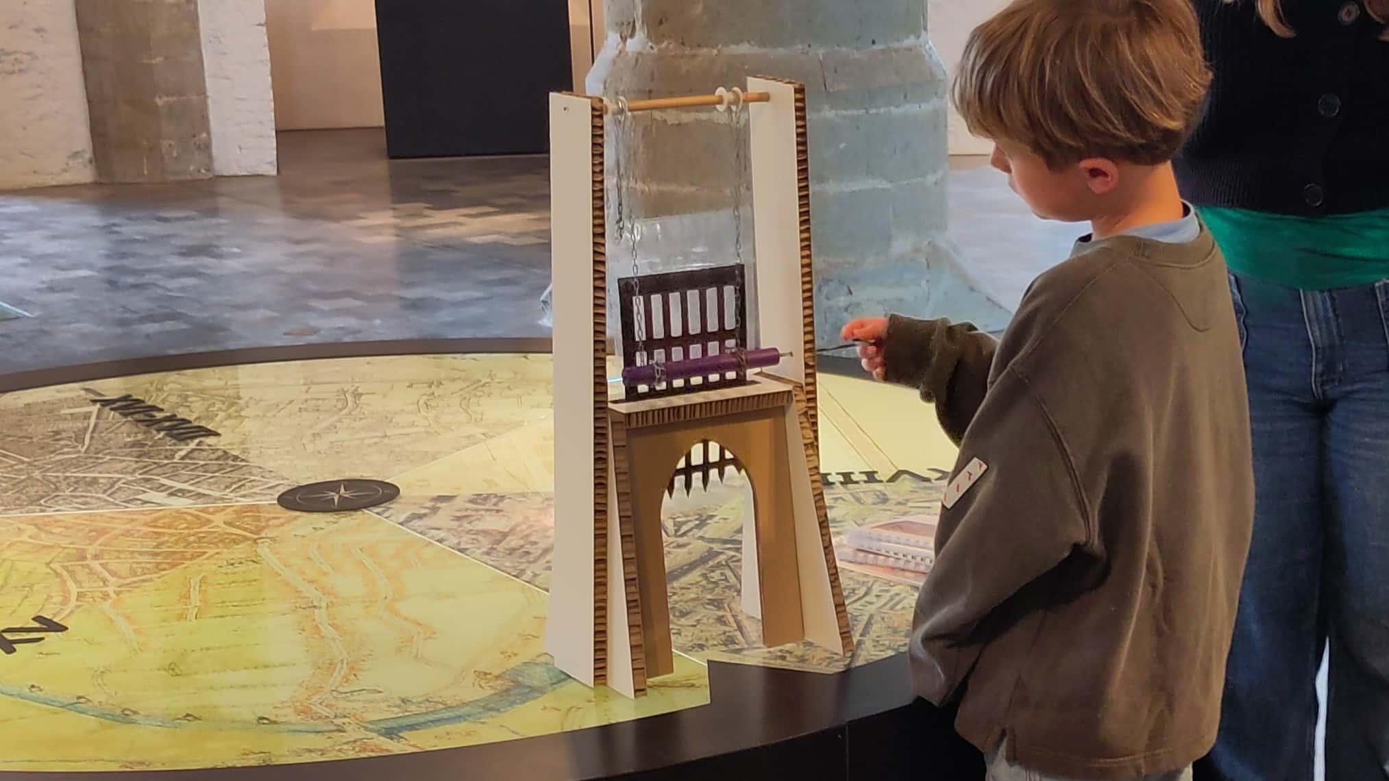 Een leerling bedient een miniatuur valhek in een museum.