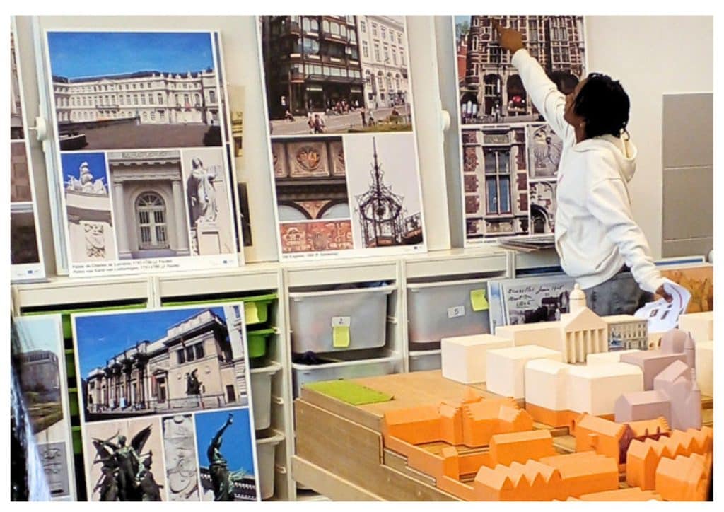 Un élève pointe du doigts des photos du quartier Royal. Il se trouve à côté d'une maquette du Mont des Arts
