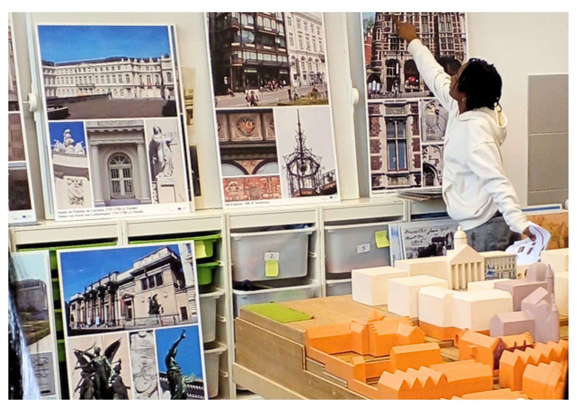 Un élève pointe du doigts des photos du quartier Royal. Il se trouve à côté d'une maquette du Mont des Arts